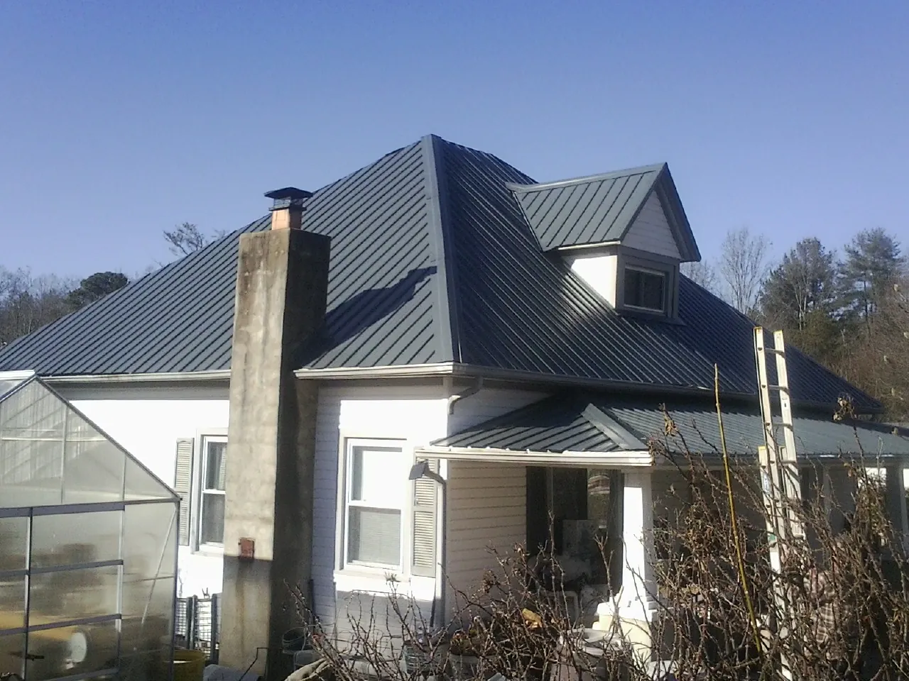 Dark blue standing seam metal roof on a white farmhouse with dormer — Slate & Tile Roof Repair by Roofing Brothers in East Jewett