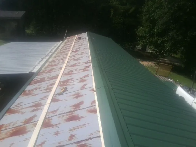 Old rusted panels beside newly installed green metal roofing — Wind Damage Roof Repair by Roofing Brothers in East Jewett