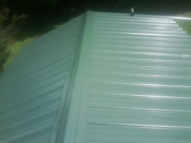 New green metal panels meeting at the ridge of a roof — Flat Roof Repair work by our crew in East Jewett