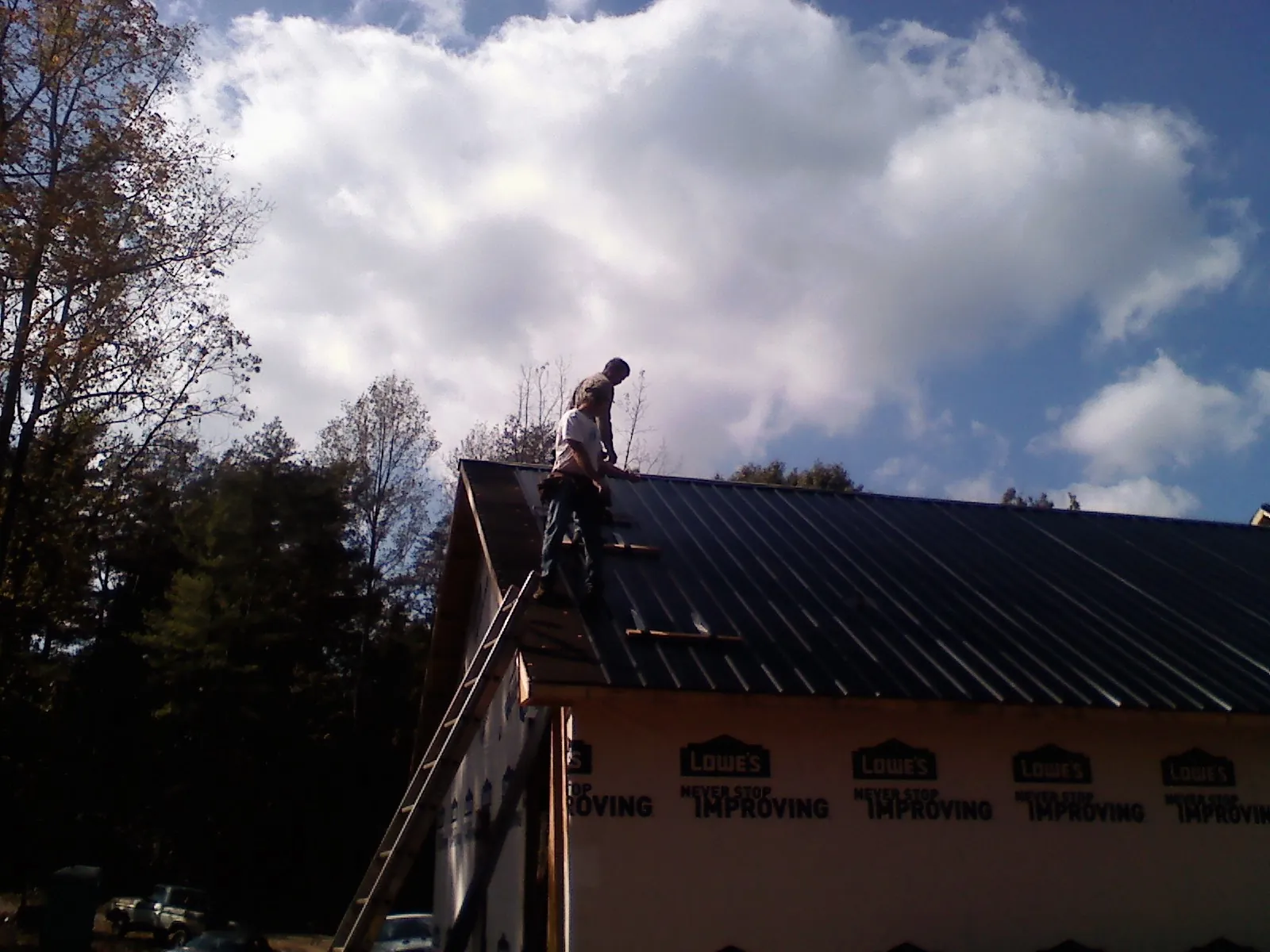 Roofer fastening dark metal panels high against a cloudy sky, from a Roof Inspection job in East Jewett