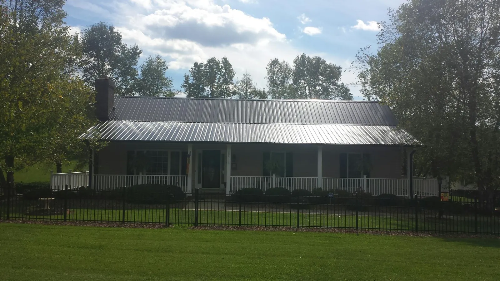 Gray metal roof on a brick ranch with a full width front porch — Gutter Guard Installation work by our crew in East Jewett