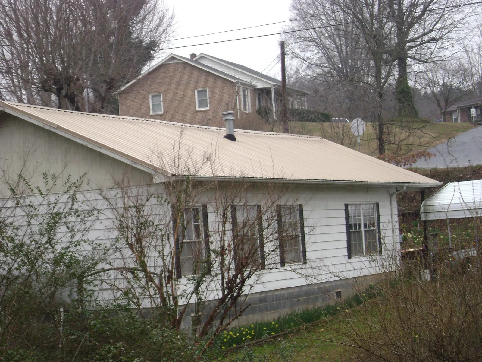 Tan metal roof on a white sided house set into a hillside — Commercial Roofing by Roofing Brothers in East Jewett